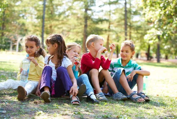 Portrait of happy friends sitting on the ground in park and having meal time