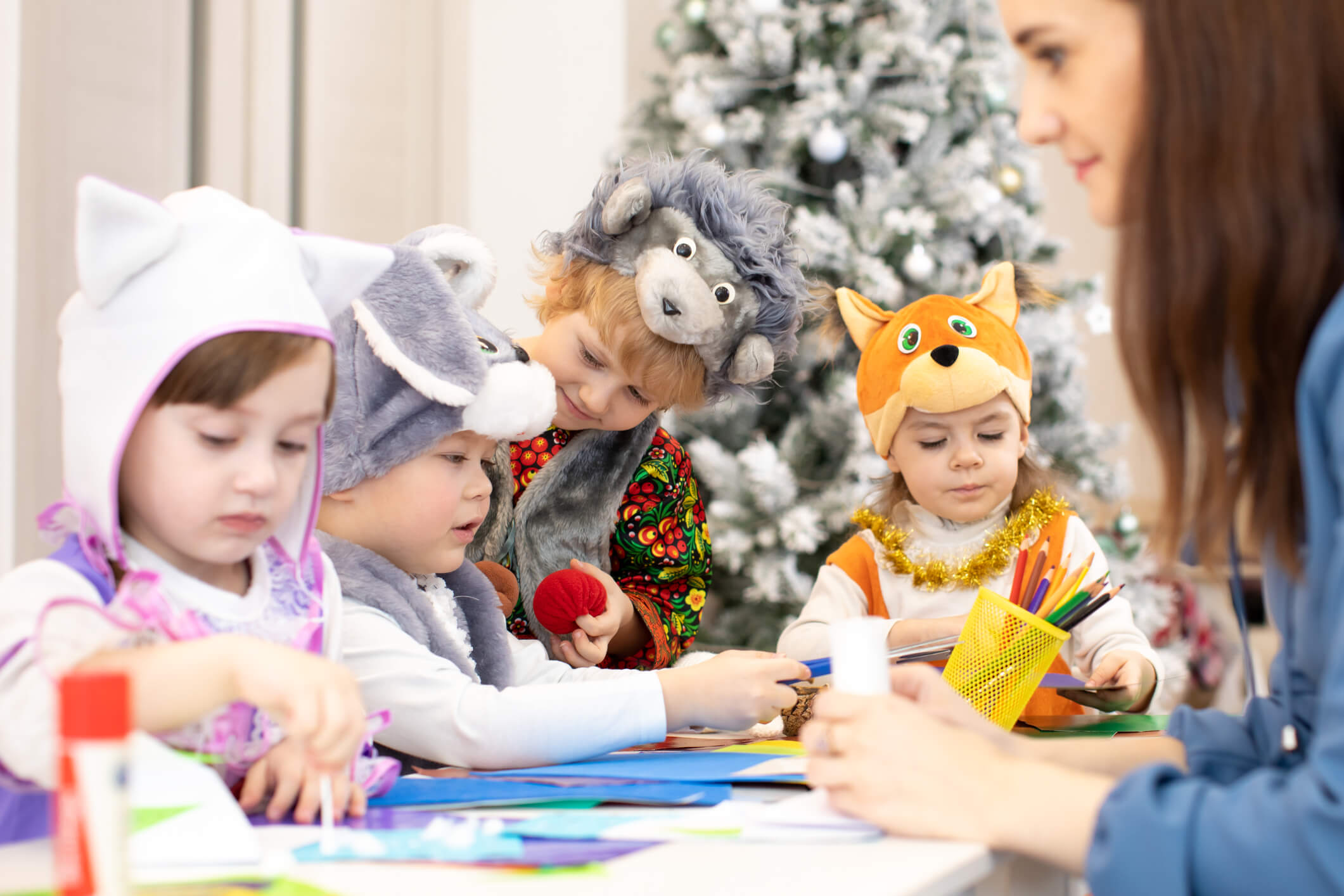 Group of preschoolers weared funny clothes on lesson in classroom. Kids with teacher make hands crafts in kindergarten. Children preparing to christmas holiday.