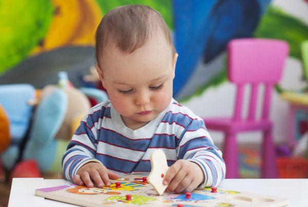 Small toddler or a baby child playing with puzzle shapes on a low table in a colorful children room in a nursery or preschool.